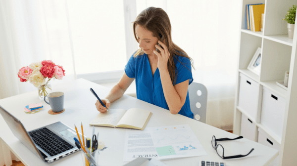 a woman in a blue dress writing on a piece of paper while working from home